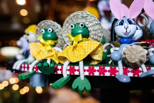 Three small handmade bird dolls in yellow dresses sit on a patterned shelf with blurred lights behind them