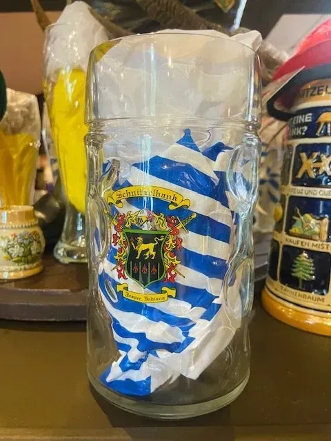 Clear glass beer stein wrapped in blue-and-white striped paper with a crest, on a shelf
