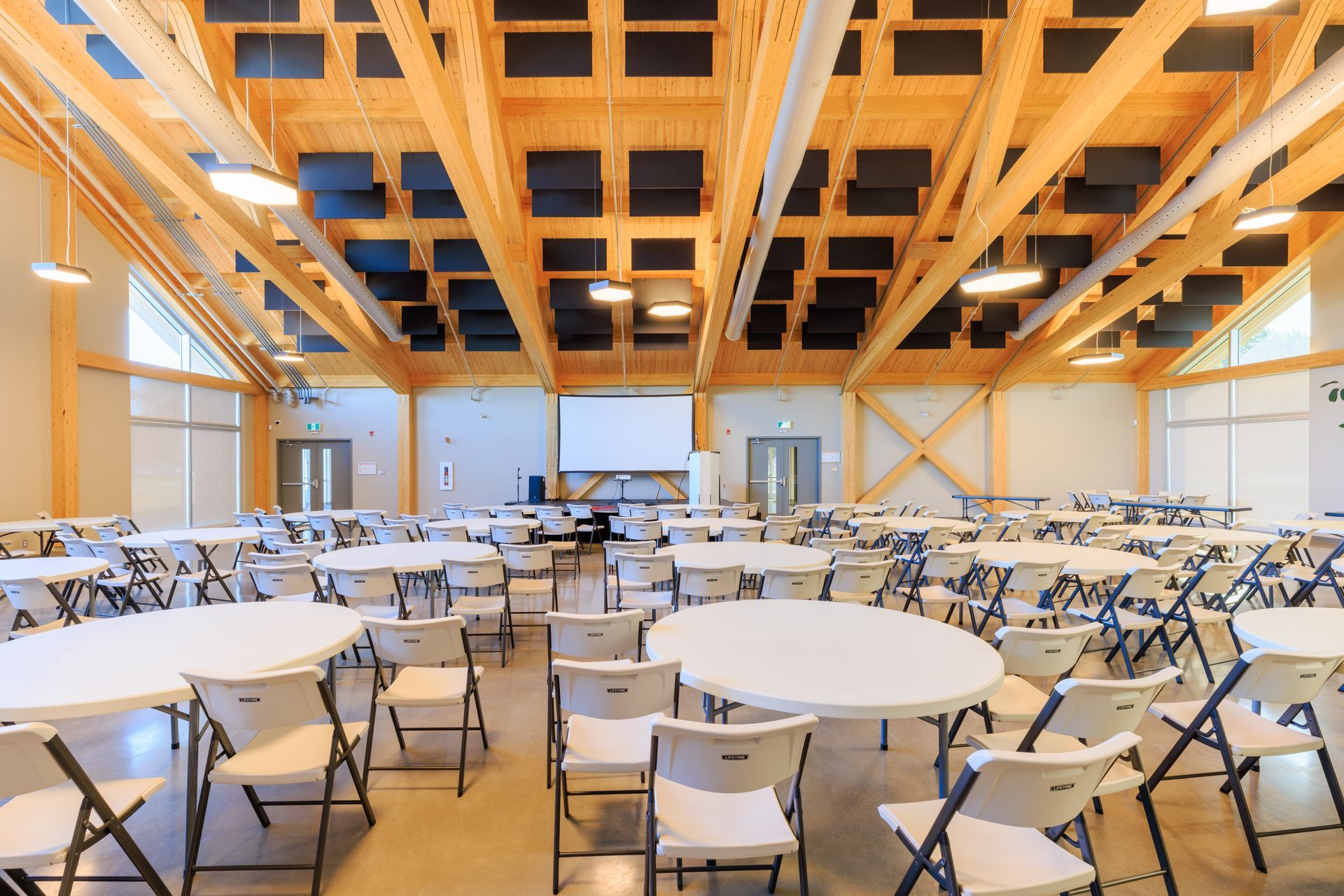 Une grande salle remplie de tables et de chaises et d'un écran de projection.