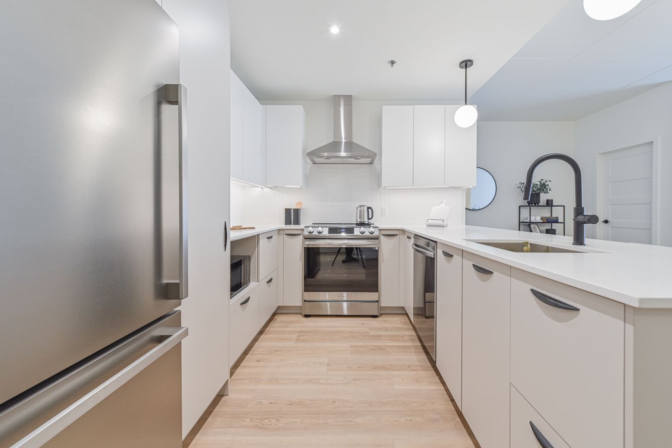 Cuisine moderne blanche avec électroménagers en acier inoxydable, plancher en bois clair et îlot central.