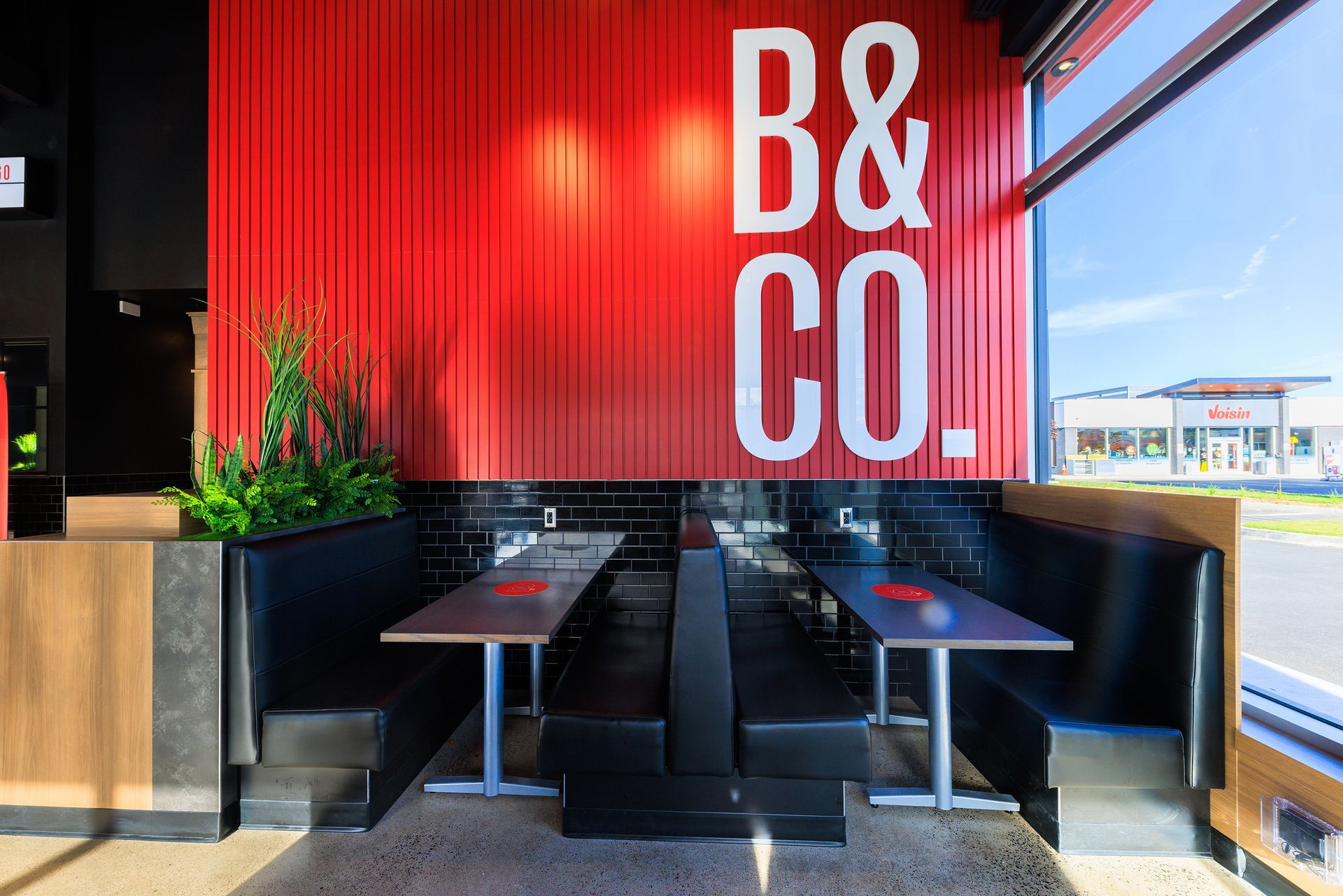 Un restaurant avec des tables et des bancs et un mur rouge avec les mots « b & co. » écrits dessus.