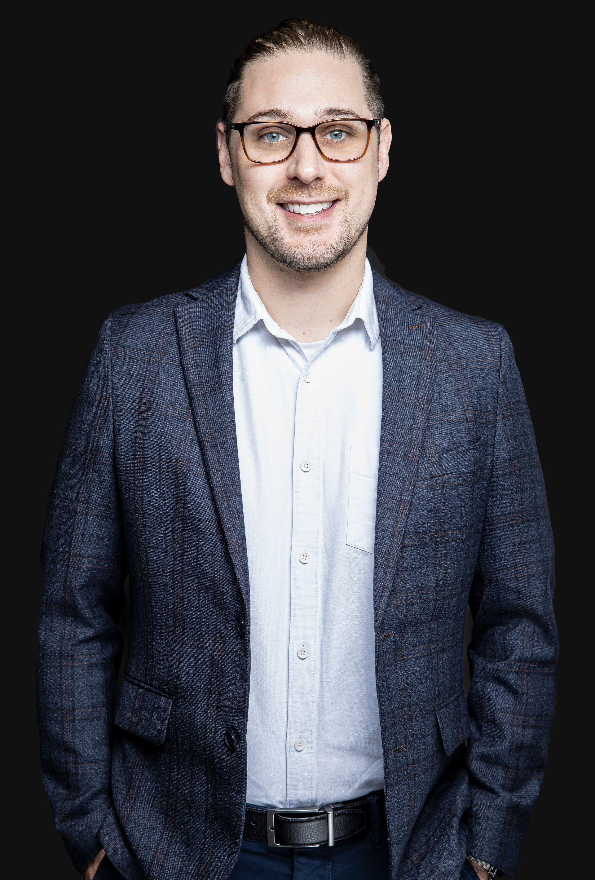 Un homme en costume et lunettes est debout avec ses mains dans ses poches.