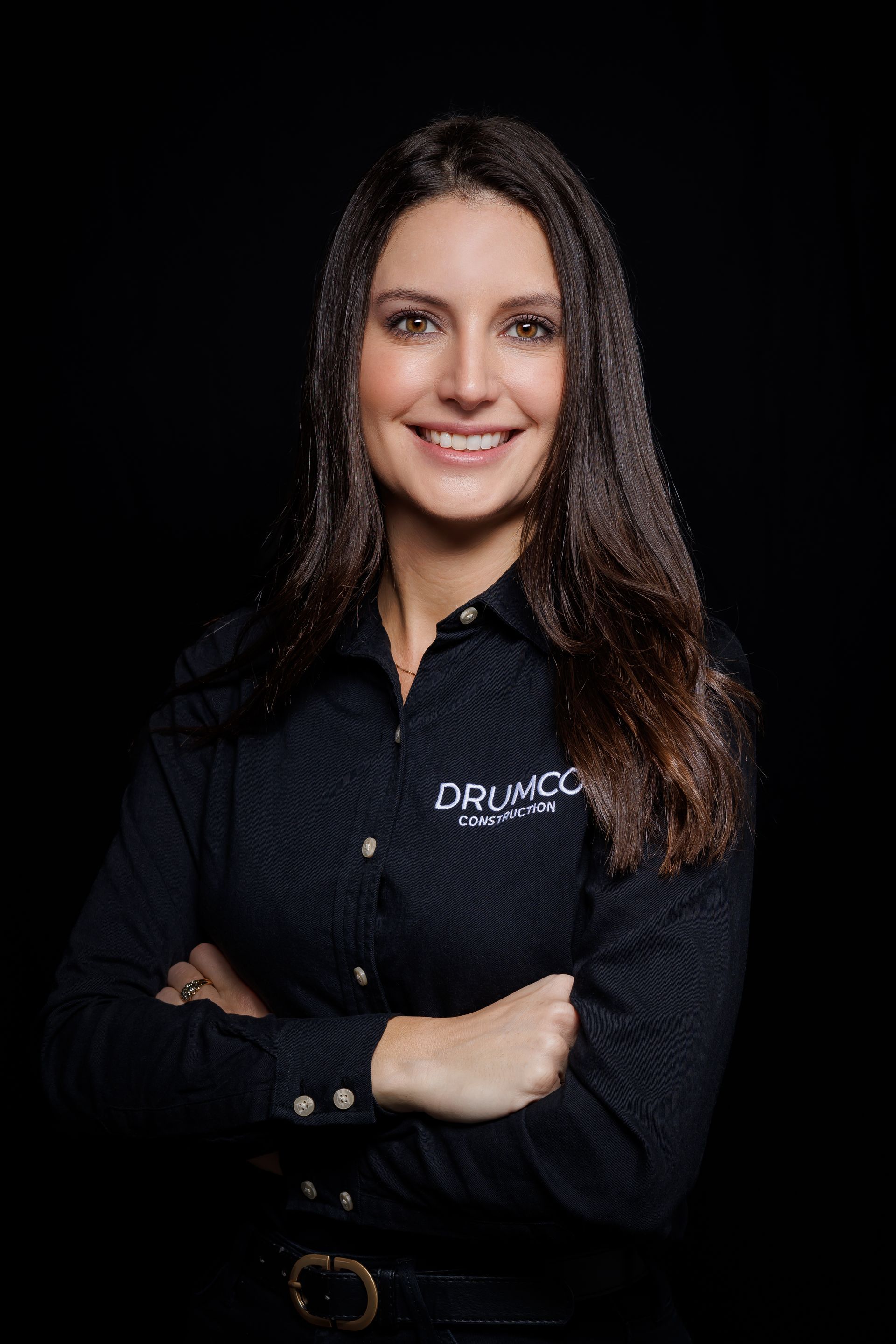 Une femme en chemise noire sourit avec les bras croisés.