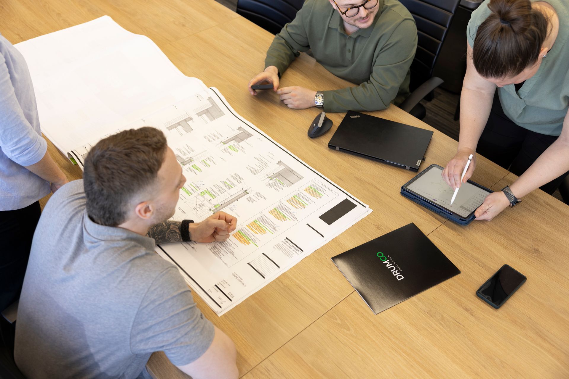 Quatre personnes à une table examinent un grand plan. Une personne utilise une tablette avec un stylet.