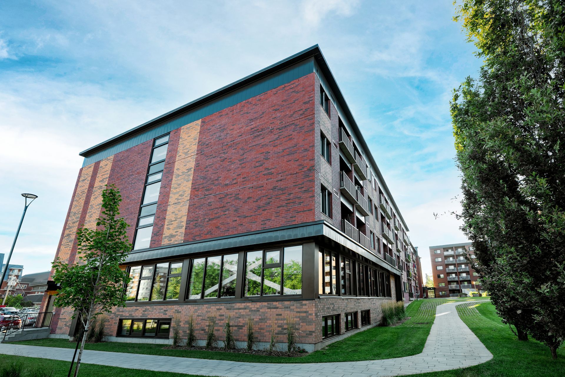 Un grand bâtiment en briques avec beaucoup de fenêtres est entouré d'arbres et d'herbe.