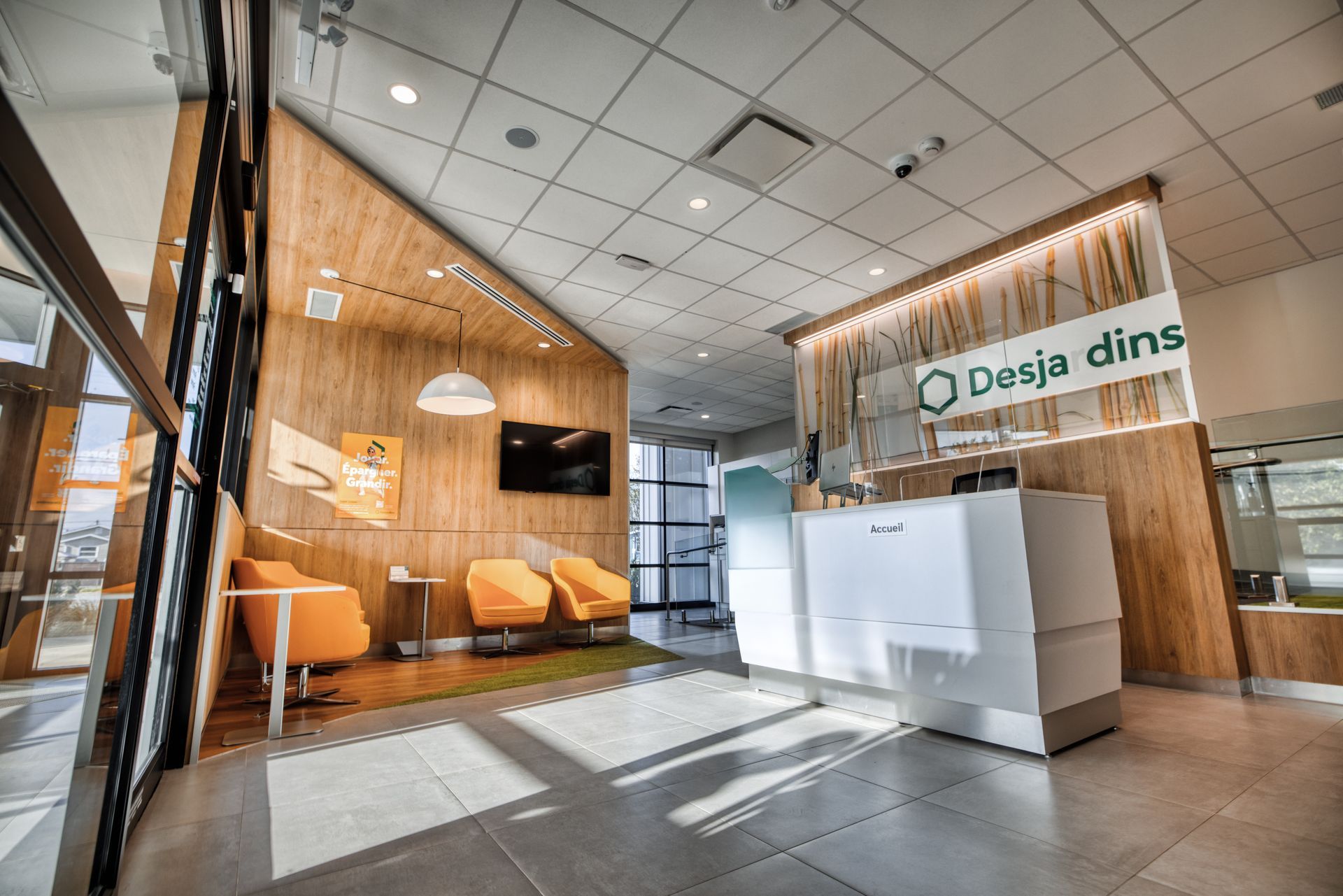 Intérieur d'une banque avec boiseries, mobilier moderne et un comptoir de réception avec le logo de la banque.