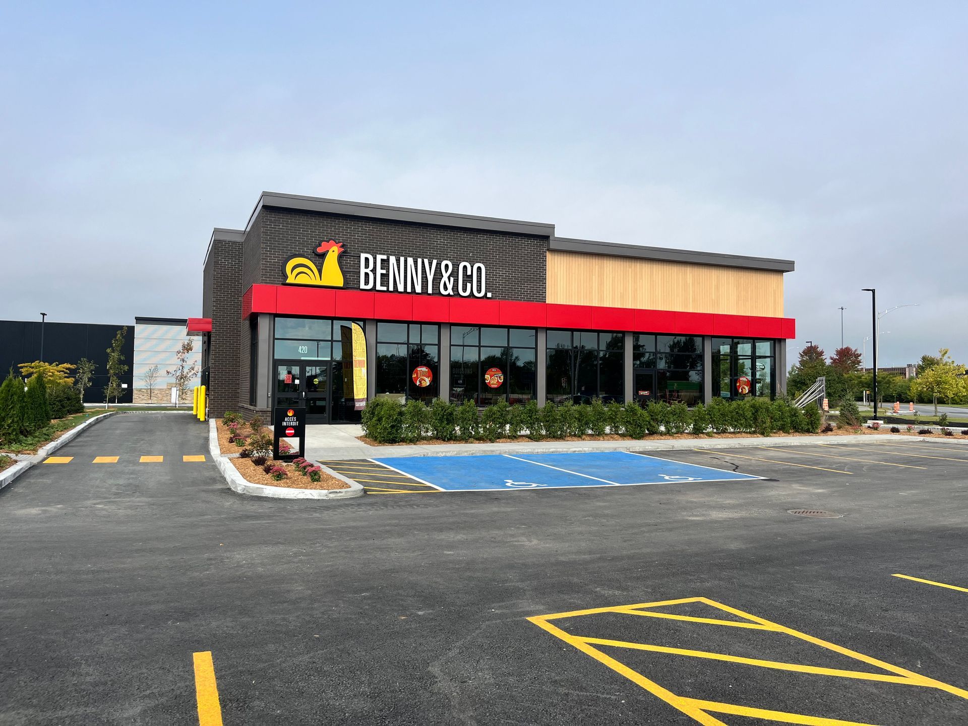Extérieur d'un restaurant Benny & Co., avec des touches de rouge, un toit noir et un service au volant.