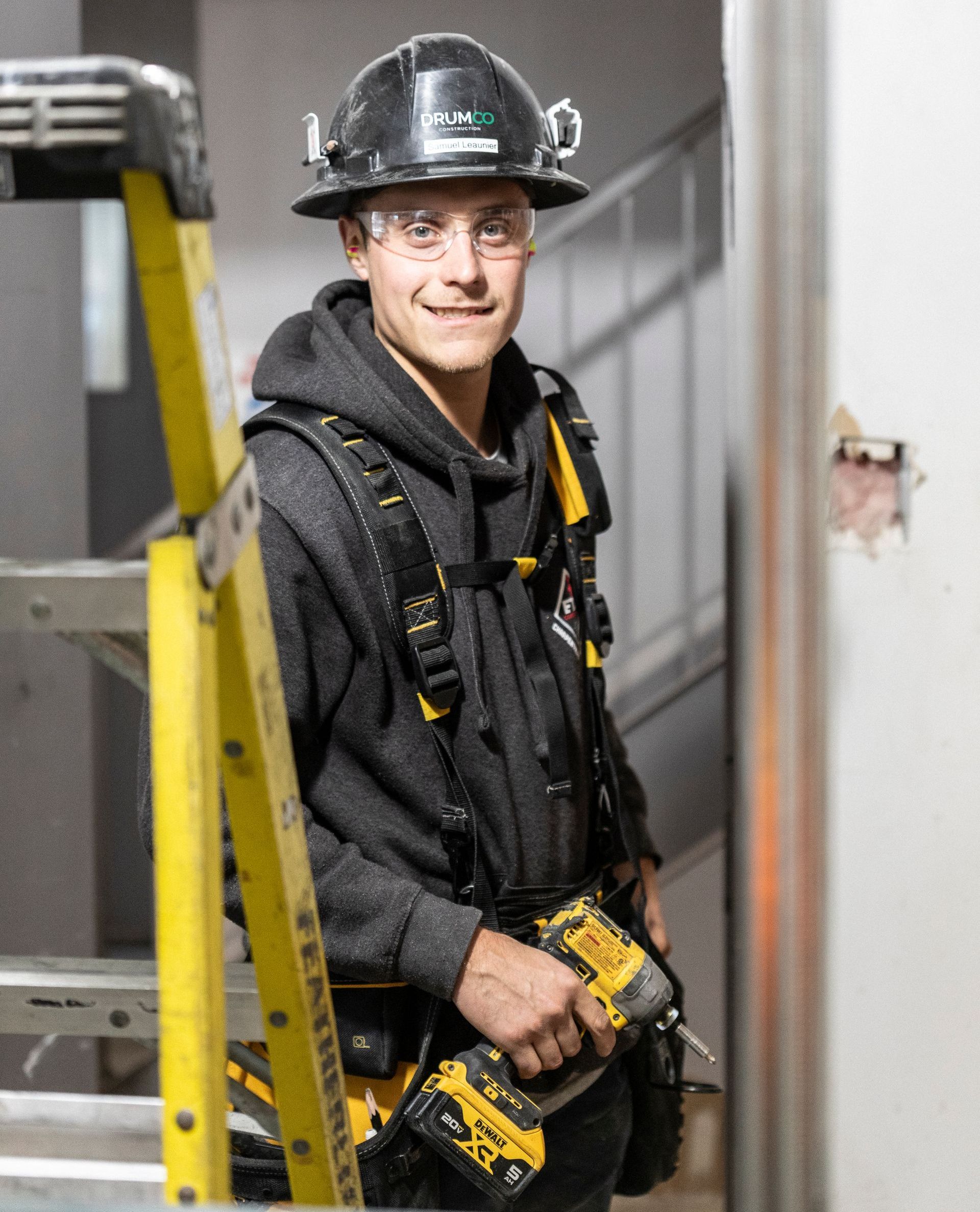 Un homme portant un casque de sécurité se tient à côté d'une échelle tenant une perceuse.