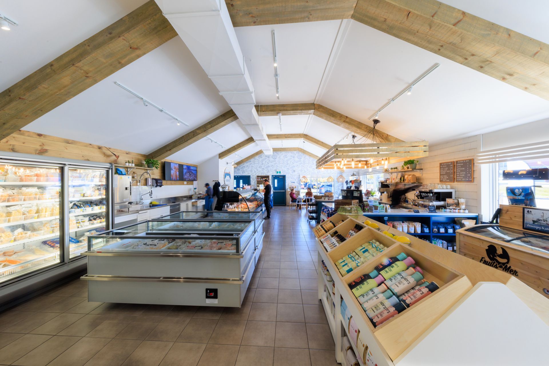 Intérieur d'un marché, avec réfrigérateurs, présentoirs et caisse. Poutres et parquet en bois clair.