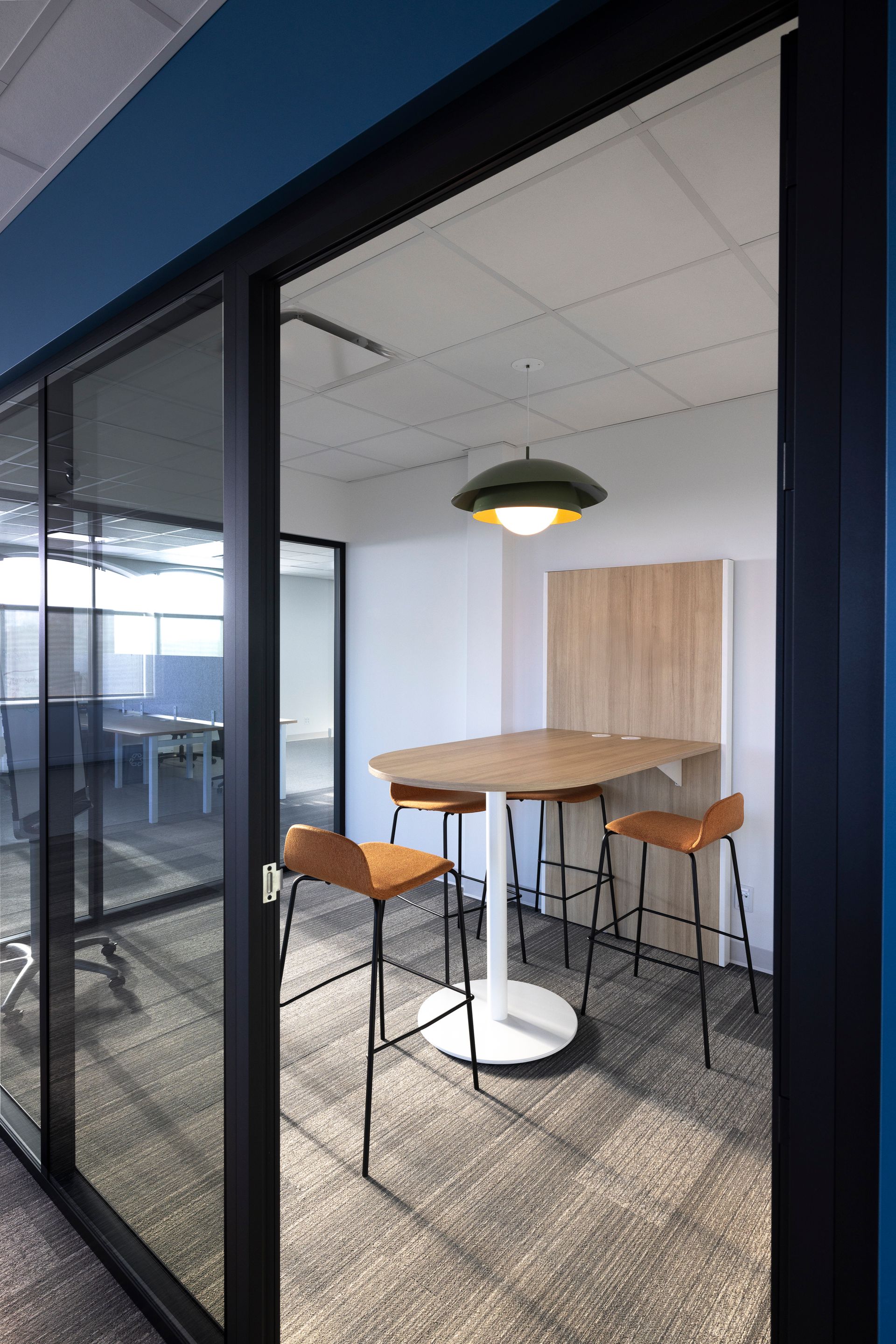 Une femme rousse travaille sur un ordinateur portable, en consultant un plan. Une tasse de café et des papiers sont posés sur la table.