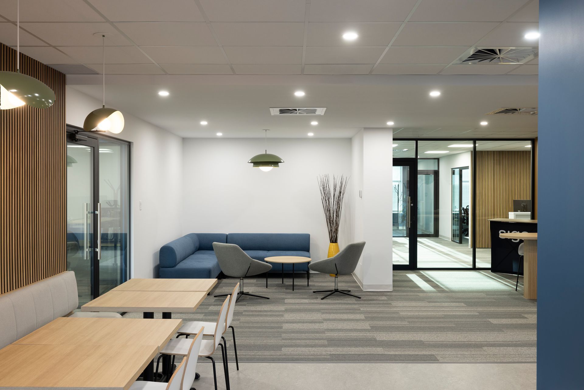 Un espace d'attente de bureau moderne avec un canapé bleu, des chaises grises et des tables en bois.