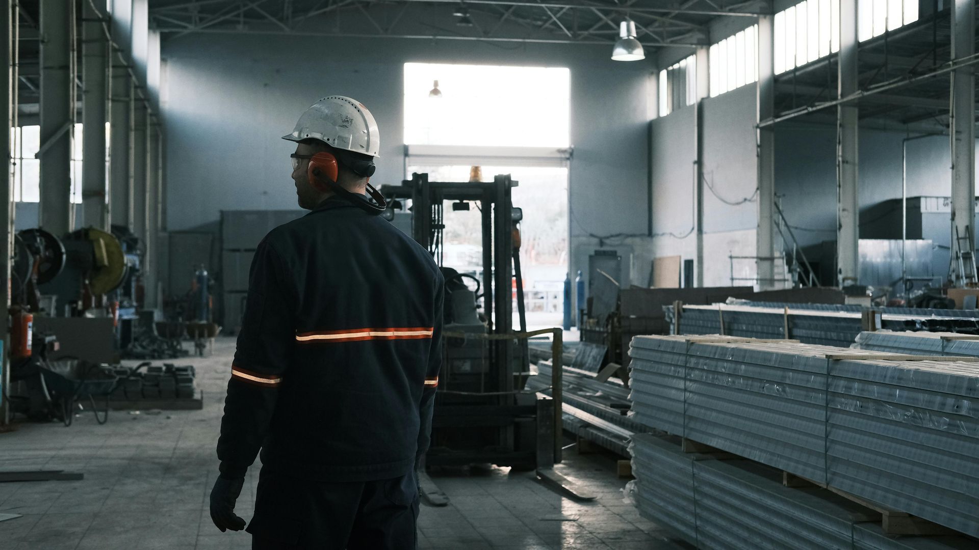 Un homme marche dans une usine avec un chariot élévateur en arrière-plan.