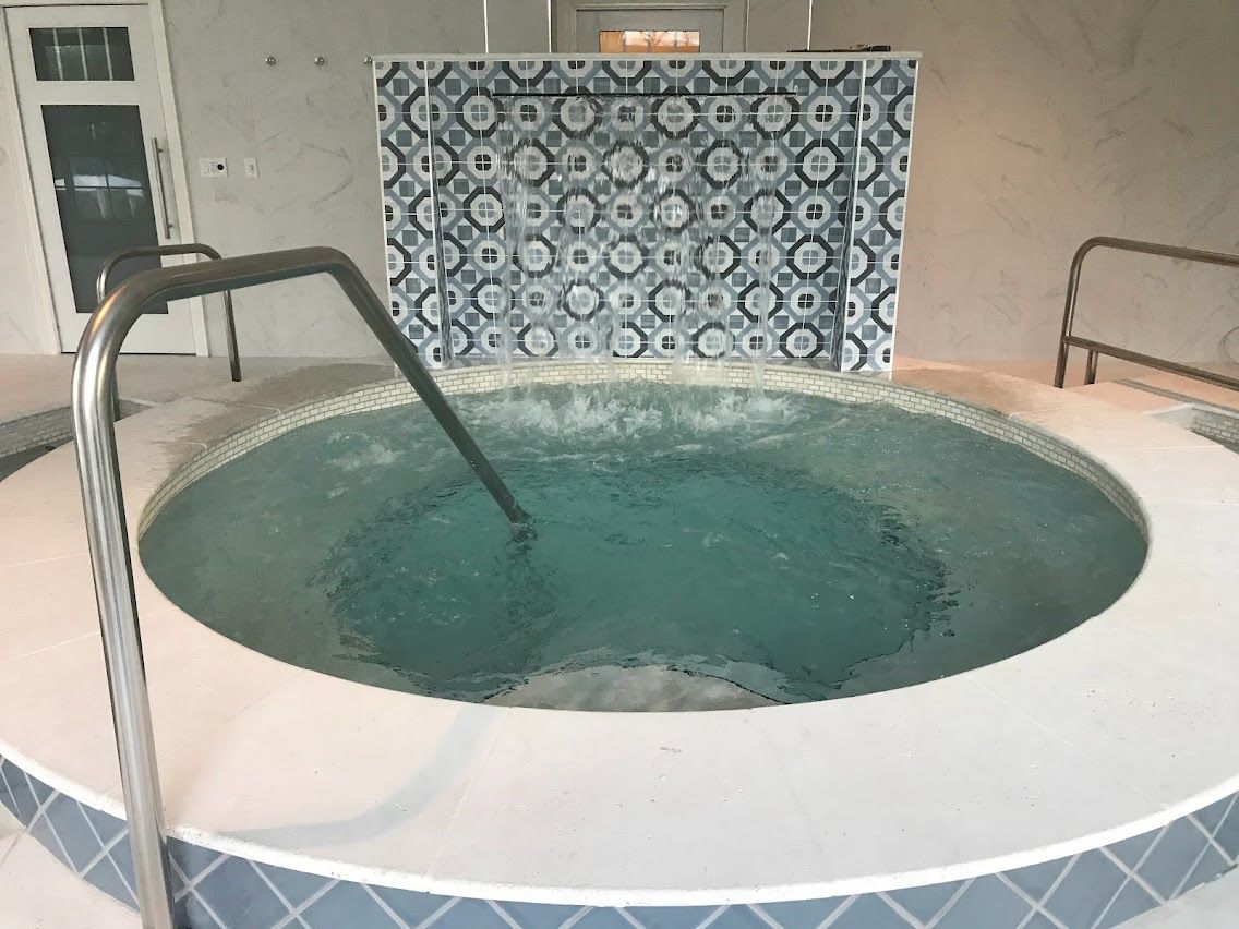 Hot tub with bubbling water, surrounded by white and patterned blue tiles, with a metal handrail.