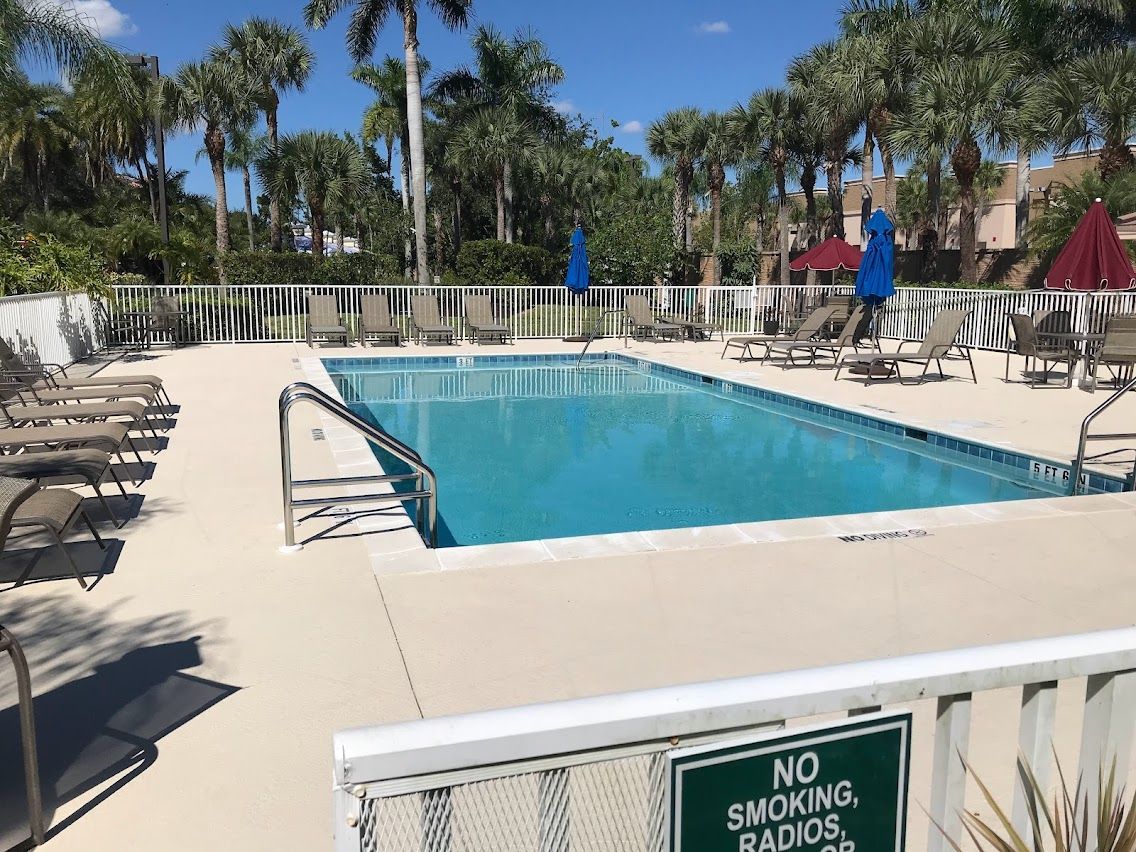 Swimming pool with lounge chairs, surrounded by a white fence and palm trees, with a 