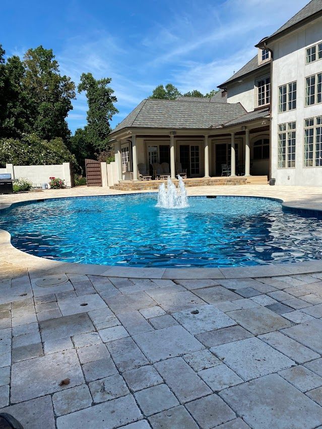Swimming pool with fountain in front of a large house with a covered patio.