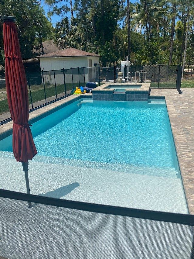 Swimming pool with attached jacuzzi, umbrella, and patio.