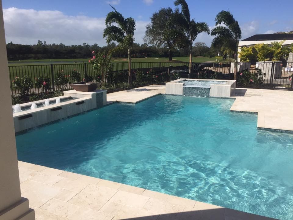 Swimming pool with turquoise water, beige tile, and a small waterfall feature under a sunny sky.