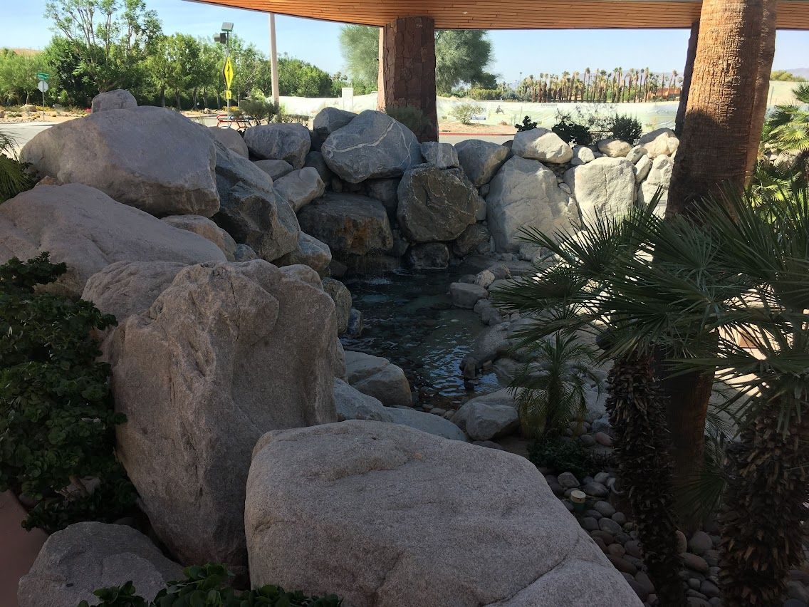 Small rock waterfall feature with flowing water, surrounded by boulders and greenery.