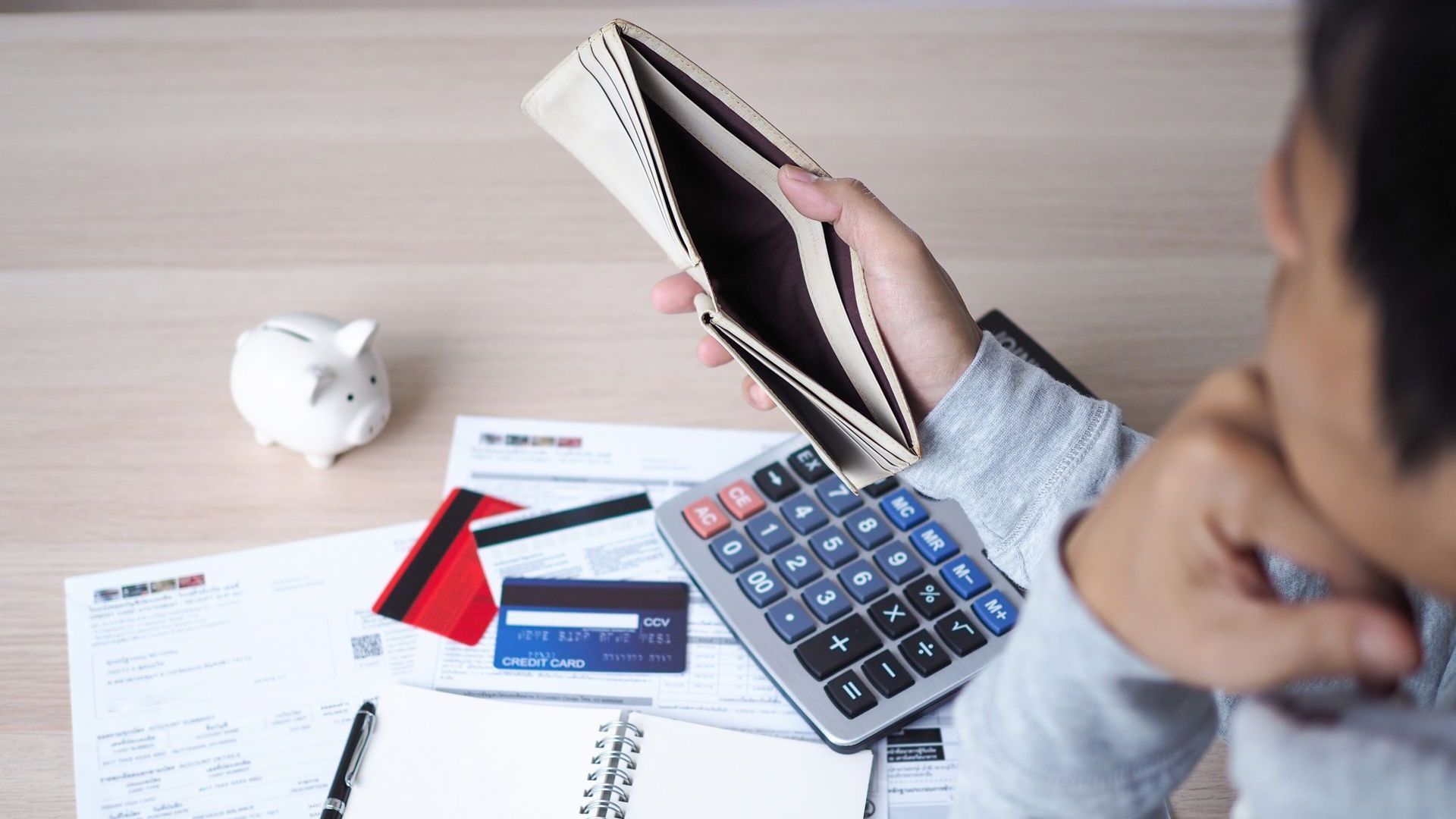 A man is sitting at a table holding an empty wallet and a calculator.