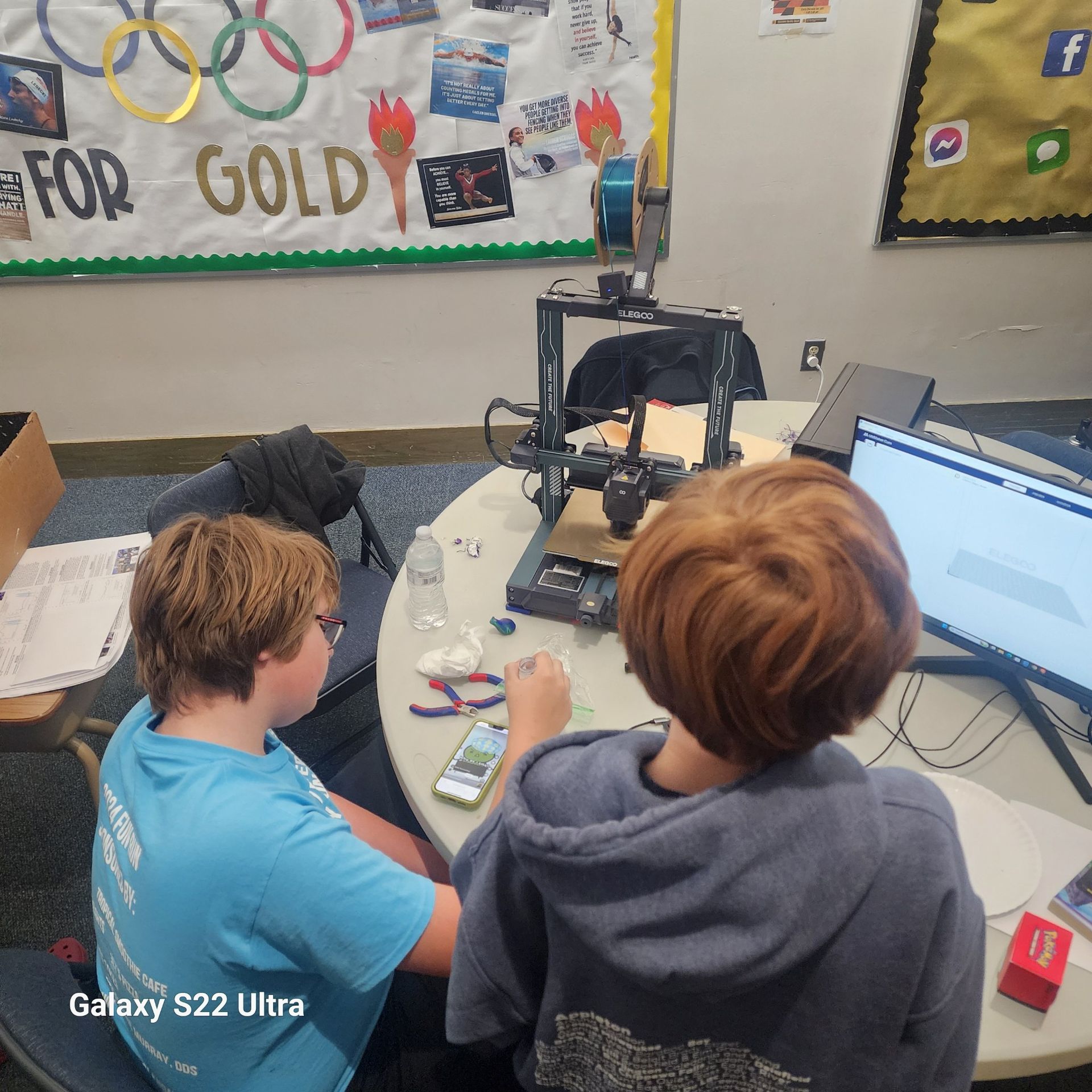 Two boys sit at a table with a galaxy s21 ultra in front of them