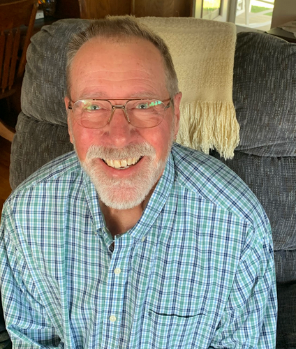 A man wearing glasses and a plaid shirt is smiling for the camera