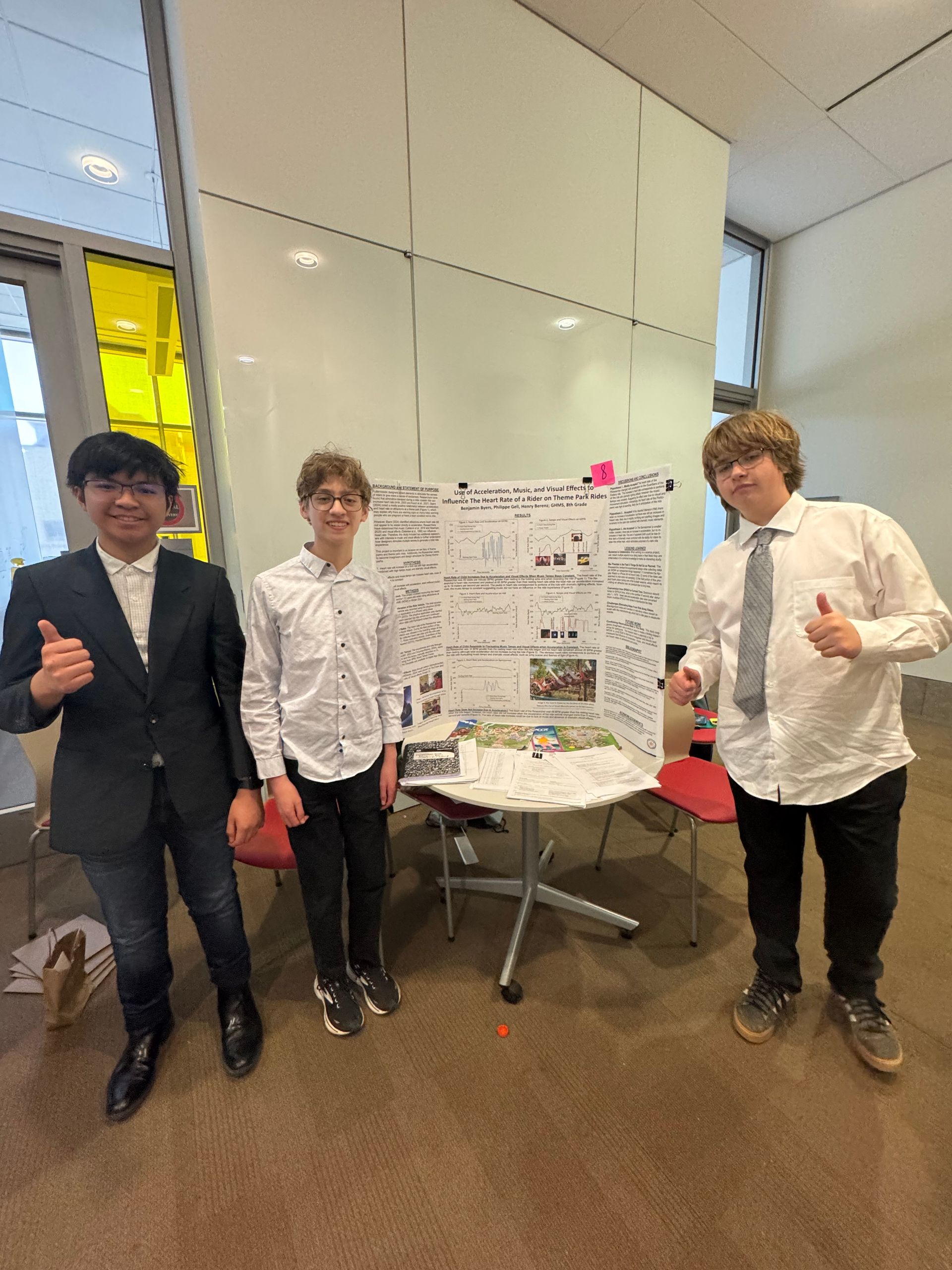 Three young men are standing in front of a poster board giving a thumbs up