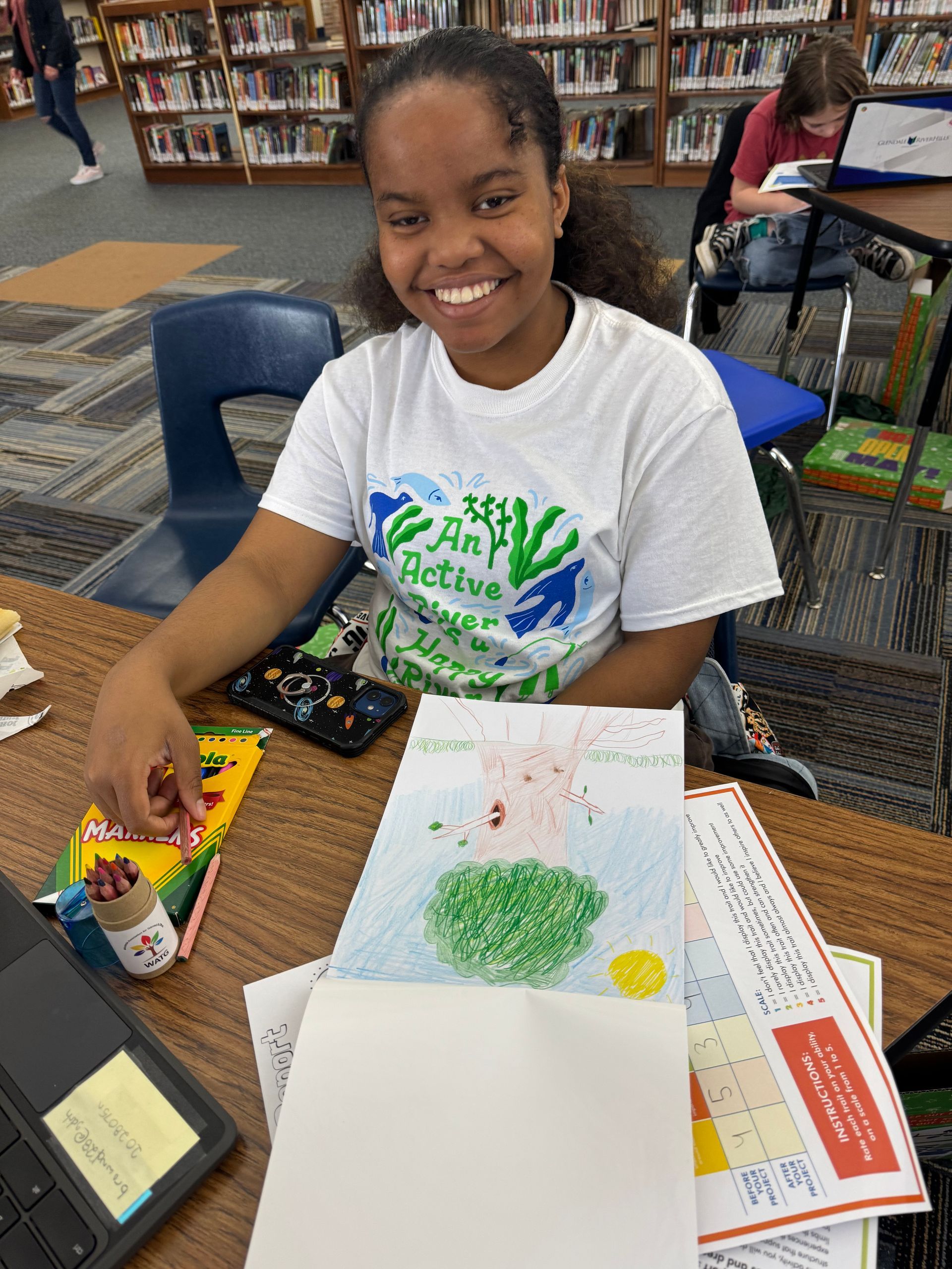 A girl is sitting at a table with a drawing of a tree on it