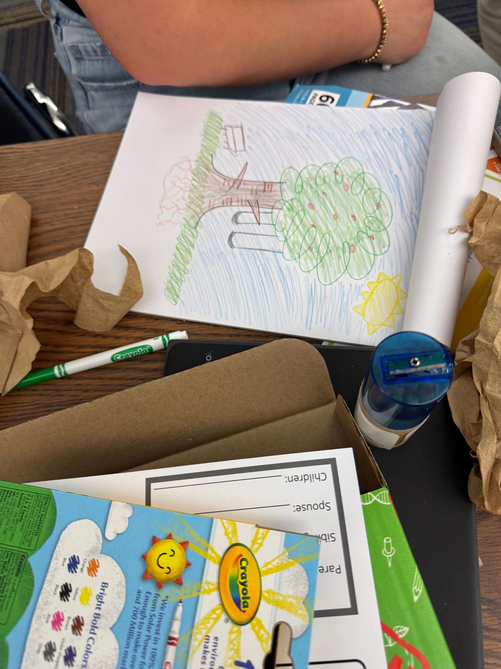 A child is sitting at a desk with a drawing of a tree on it
