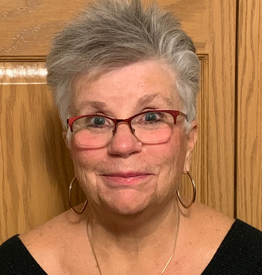 A woman wearing glasses and hoop earrings is smiling for the camera.