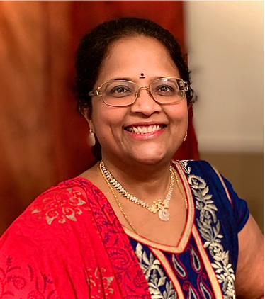 A woman wearing glasses and a necklace is smiling for the camera.