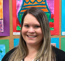 A woman is smiling in front of a wall of paintings.