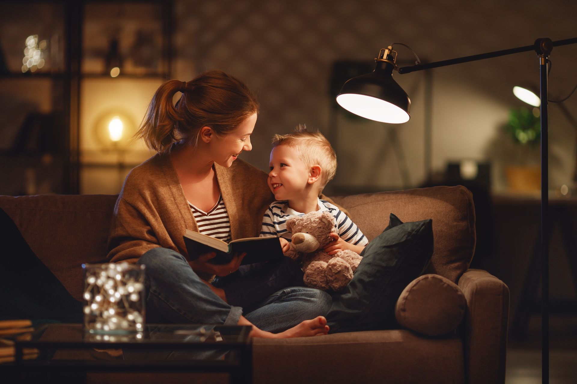 A woman and a child are sitting on a couch reading a book.