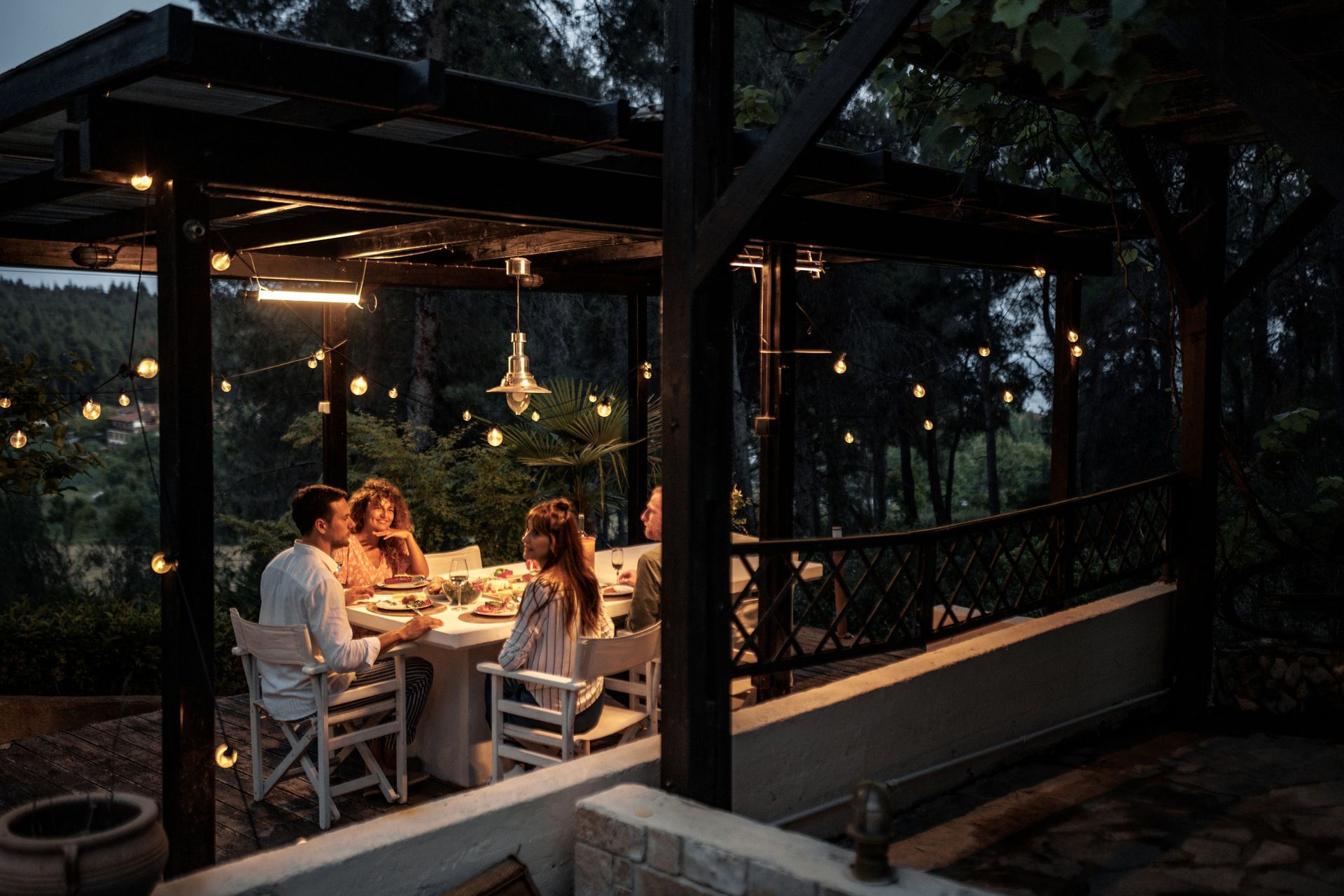 A group of people are sitting at a table under a pergola at night.