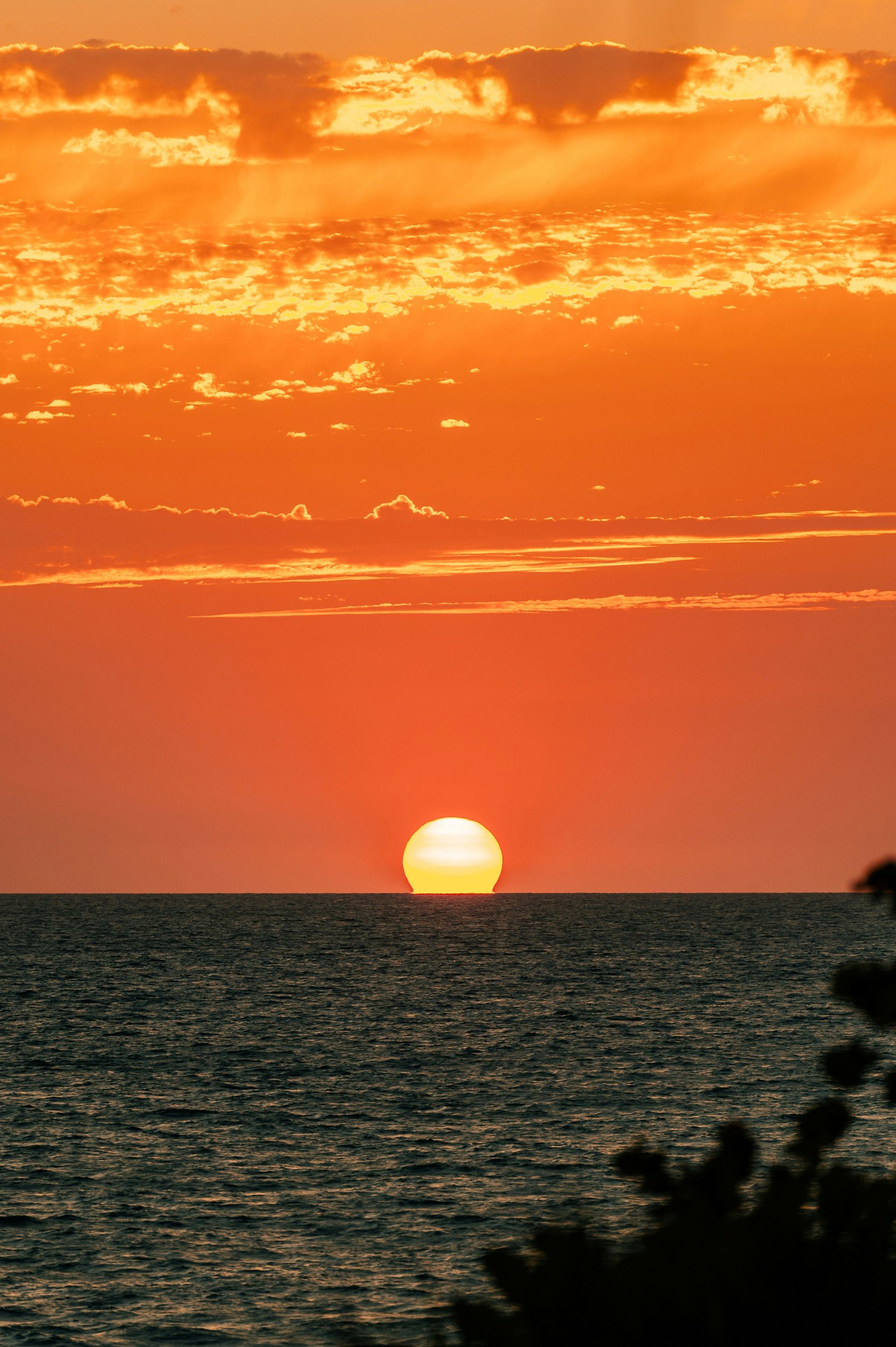 Sunset over the ocean; the sun is a bright orb on the horizon, and the sky is filled with orange and yellow hues.