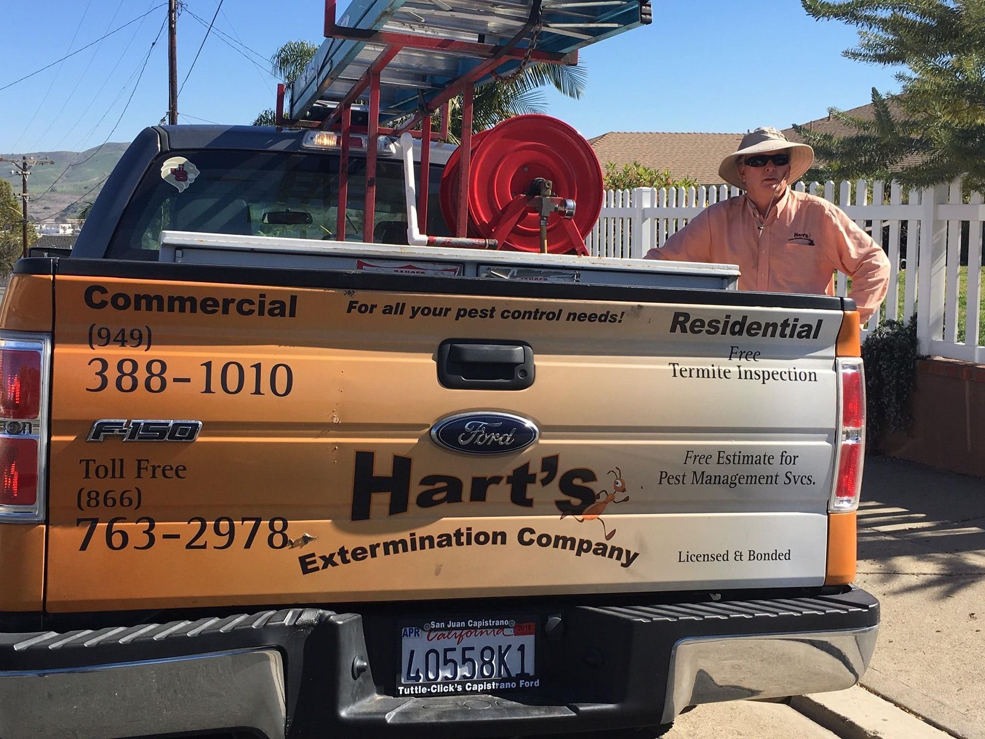 A person in a sun hat stands by the tailgate of Hart's Extermination Company's orange and white Ford pickup truck.