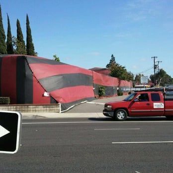 A building draped in a red and black striped tent for fumigation, with a red service truck parked on the street nearby.
