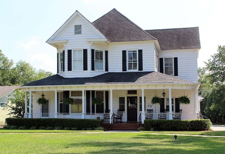 White two-story house with black shutters and a wraparound porch, set on a green lawn.