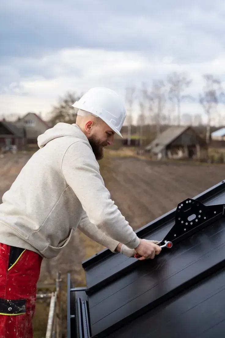 Roofer in hardhat hammers metal flashing on a residential roof in the sunlight.