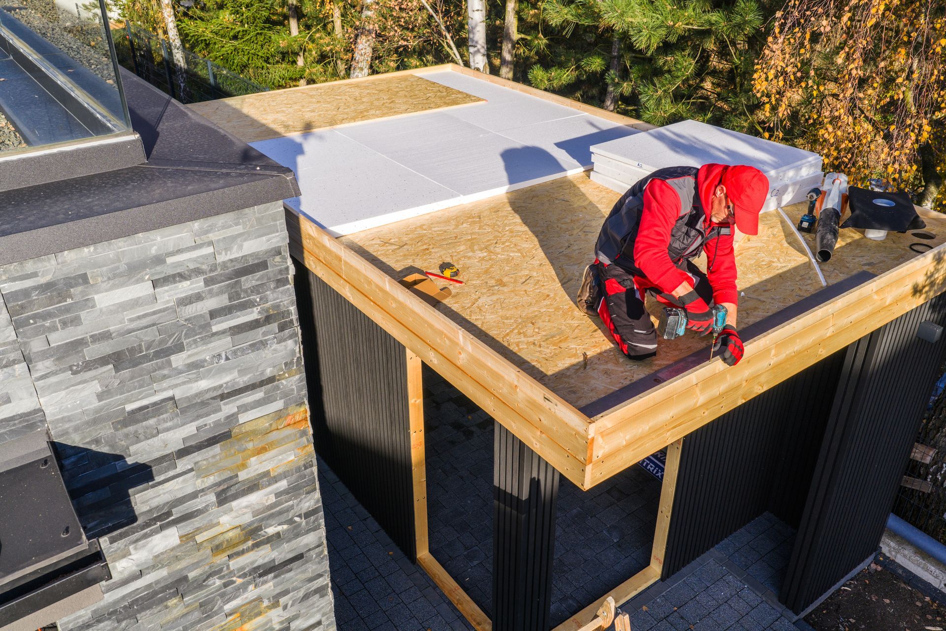 Man in orange hard hat and red overalls installing a solar panel outdoors.