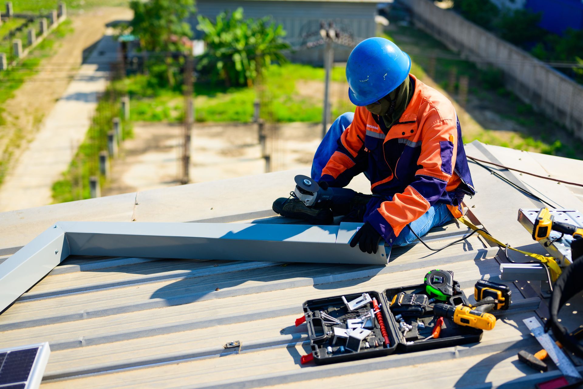Roofer in safety gear, kneeling on a rooftop, hammering shingles.