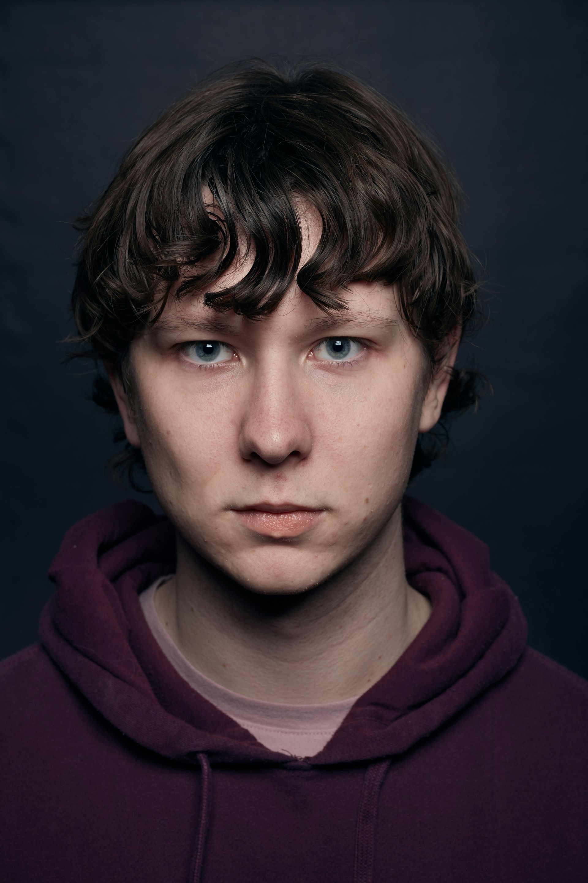 Young person with light skin and curly brown hair wearing a purple hoodie, looking straight ahead.