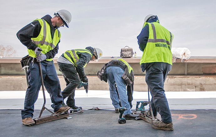 Construction worker with chainsaw and hammer, standing on a rooftop, city skyline in background.
