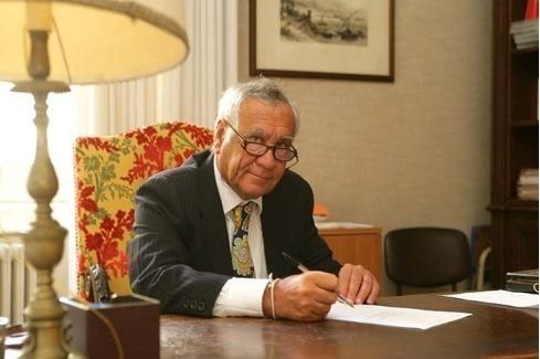 un uomo in giacca e cravatta è seduto a una scrivania e scrive su un foglio di carta .