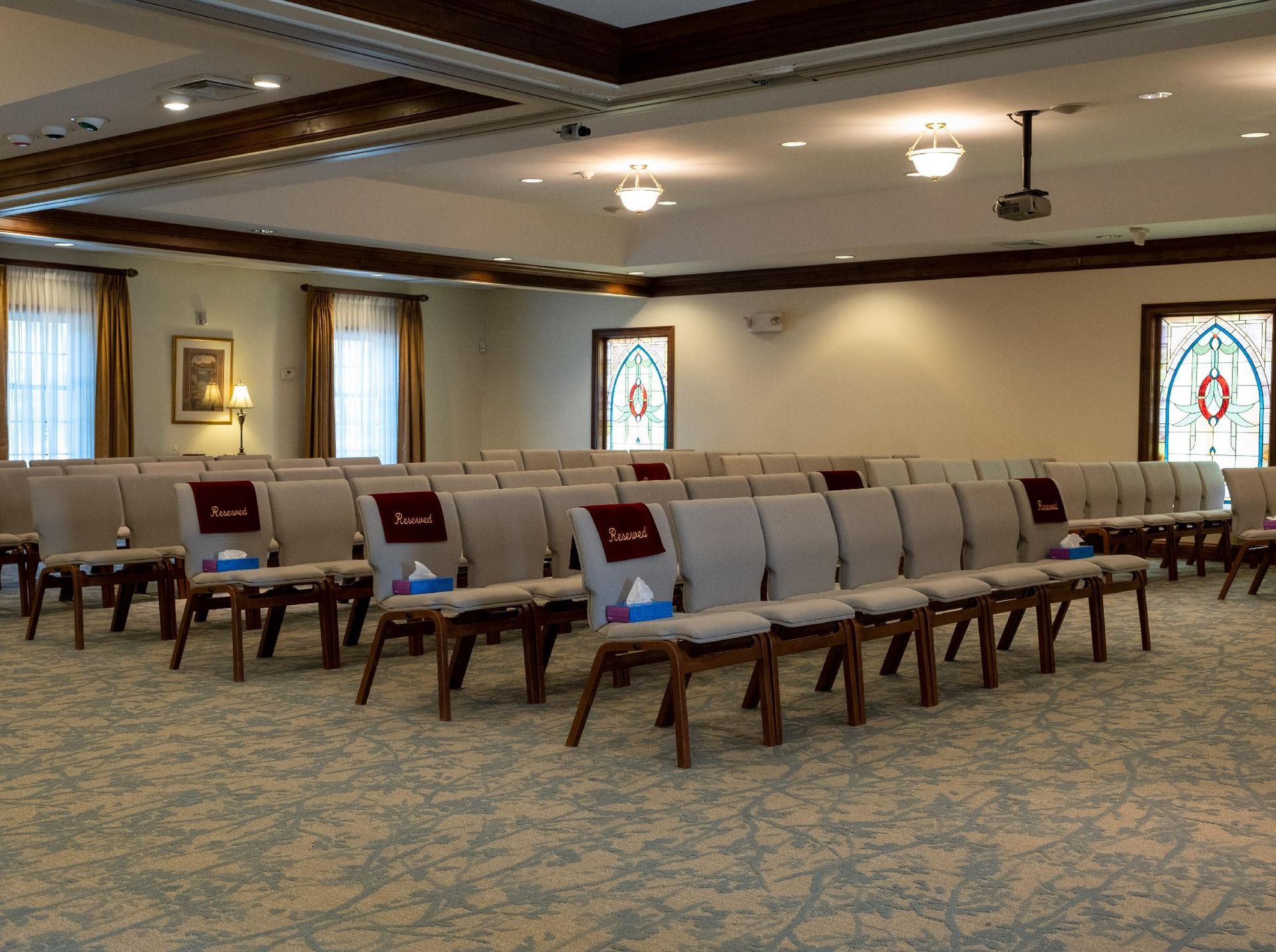 A large room with rows of chairs and stained glass windows.