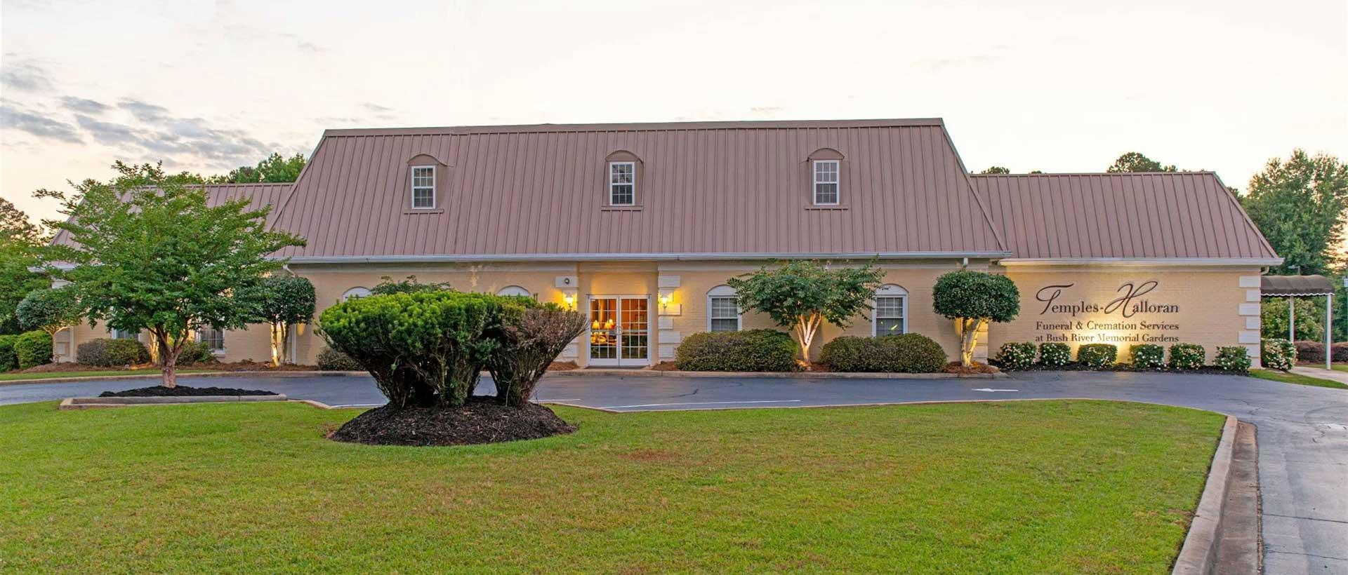 A large white house with a brown roof and a lush green lawn in front of it.