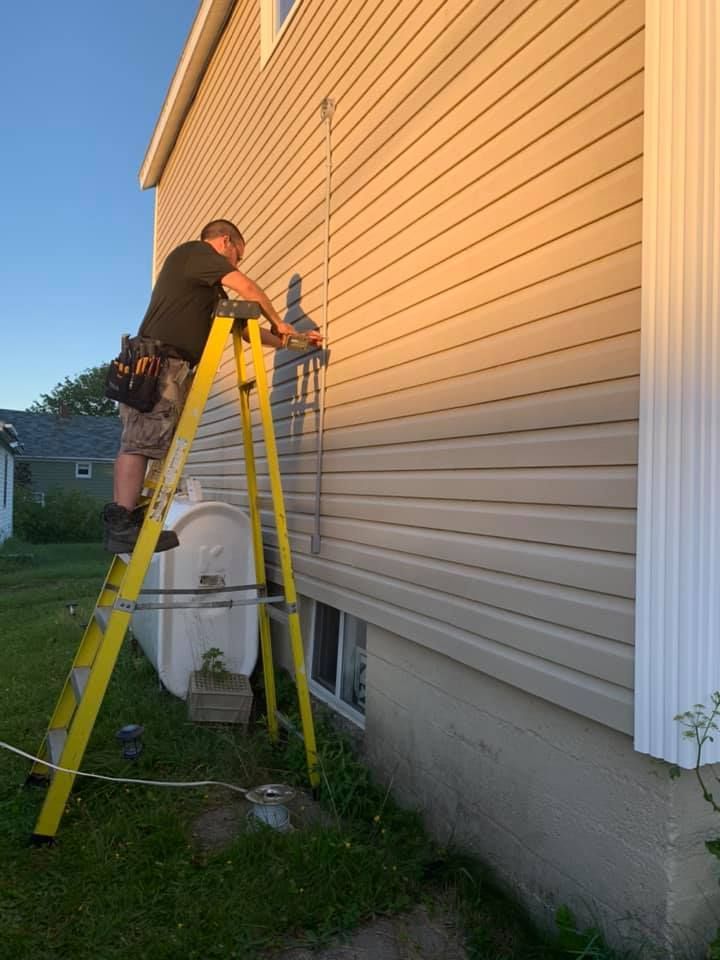 A man is standing on a ladder working on the side of a house.