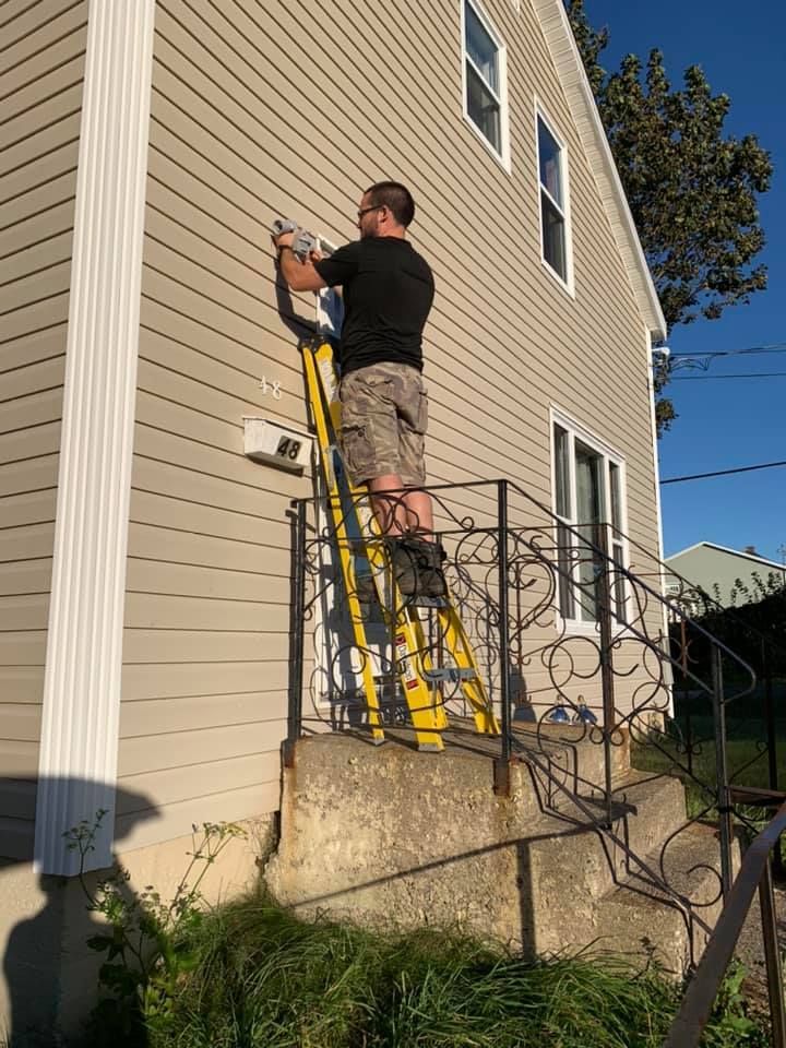 A man is standing on a ladder on the side of a house.