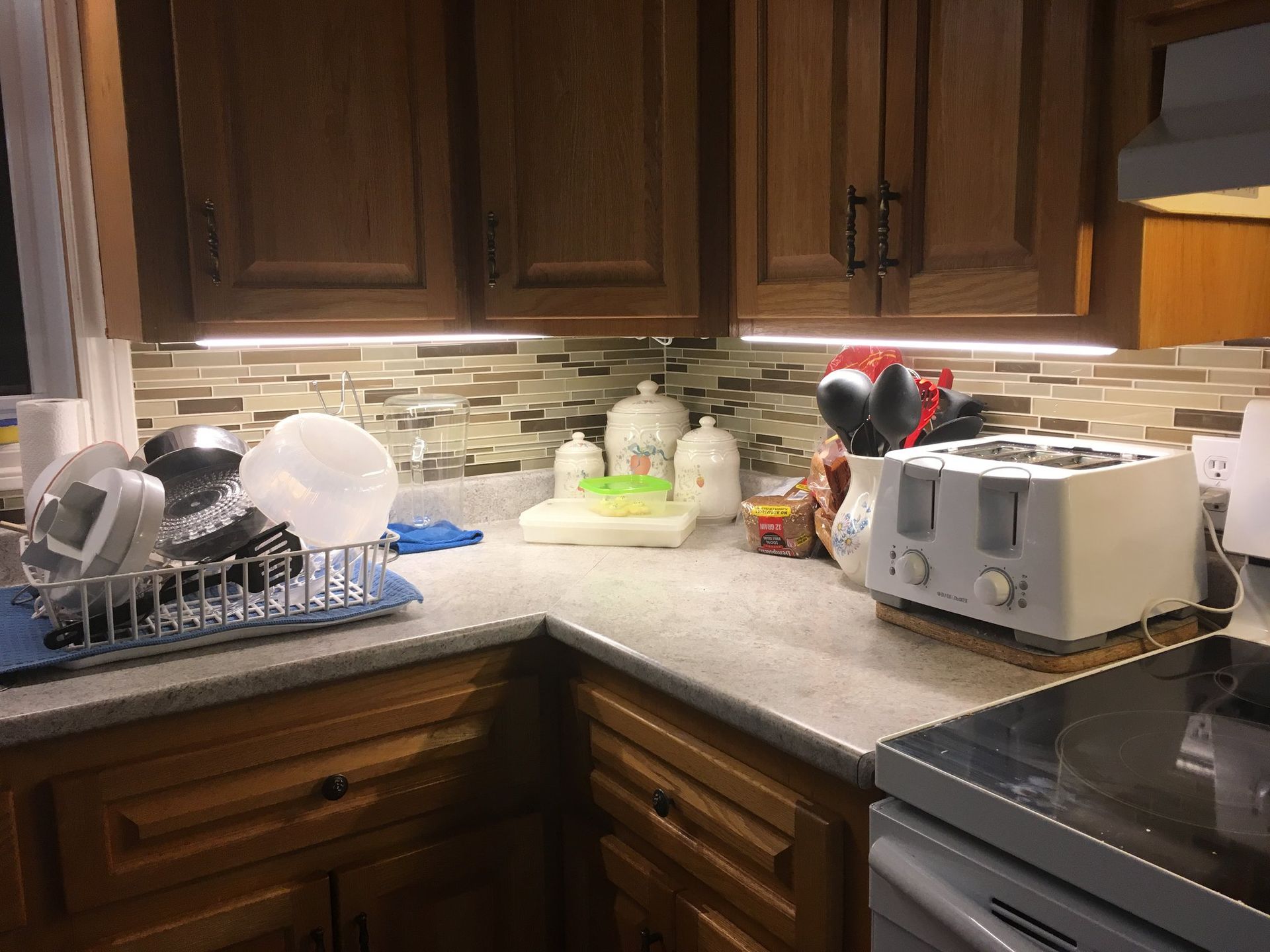 A kitchen with wooden cabinets , a toaster oven , a stove and a sink.