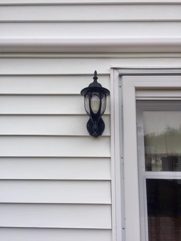A lamp is hanging on the side of a white house next to a window.