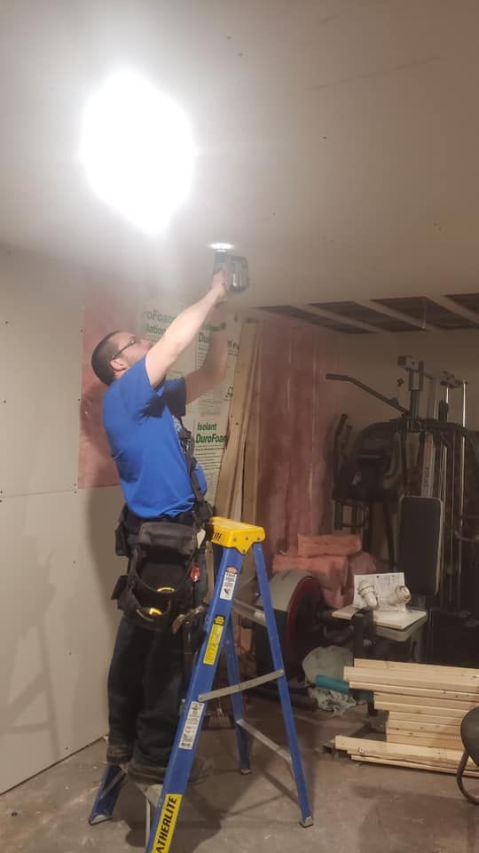 A man is standing on a ladder working on a light fixture.